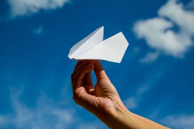 Mavi gökyüzüne karşı elinde kağıt uçak