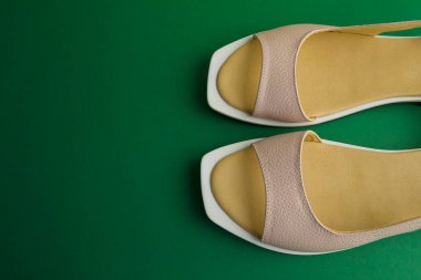 Yeşil arka planda bej renkli kadın ayakkabıları. Ayakkabılar üstten çıkarıldı.