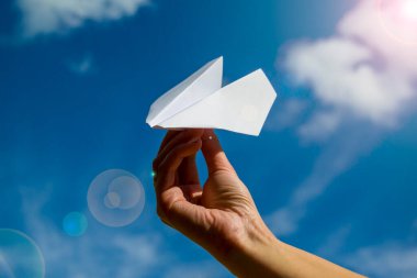 Mavi gökyüzüne karşı elinde kağıt uçak