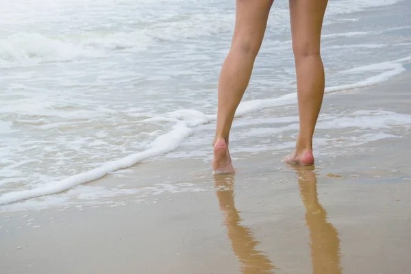 Kadınların ayakları kıyı şeridinde duruyor. Kadın deniz kumu üzerinde yürüyor.