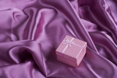 Mor saten kumaş kıvrımları üzerinde pembe kare hediye kutusu