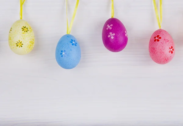 Coloridos huevos de Pascua colgando sobre fondo de madera blanca — Foto de Stock