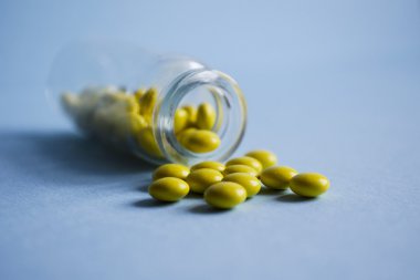 Sarı hapları bir cam kavanoz mavi zemin üzerine dışarı dökmek