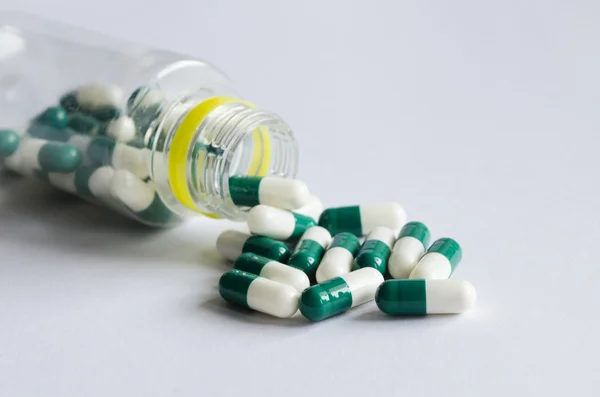 Pílulas verdes e brancas derramar de um frasco de plástico em backgr luz — Fotografia de Stock
