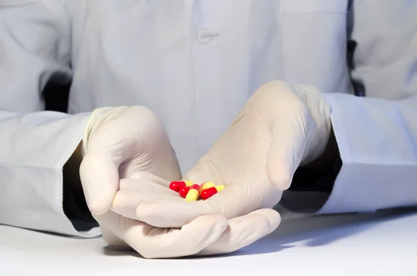 Hands in medical gloves holding red and yellow capsules — Stock Photo, Image