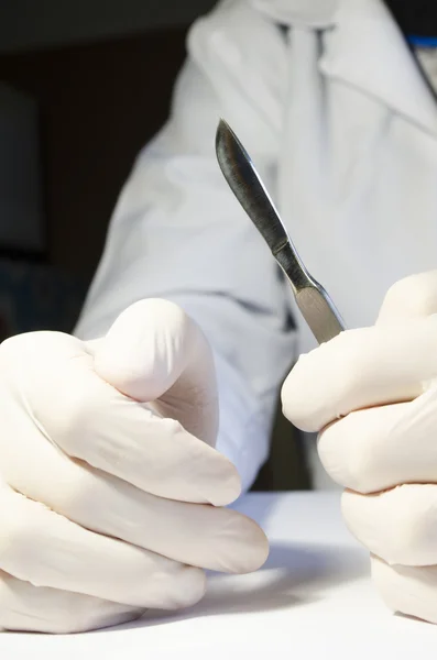 Рука крупным планом в медицинской резиновой перчатке с металлическим скальпелем — стоковое фото
