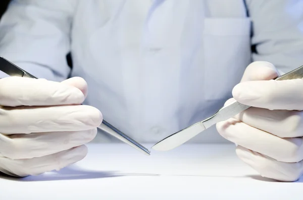 Hands in medical rubber gloves holding metal tweezers and a scal — Stock Photo, Image