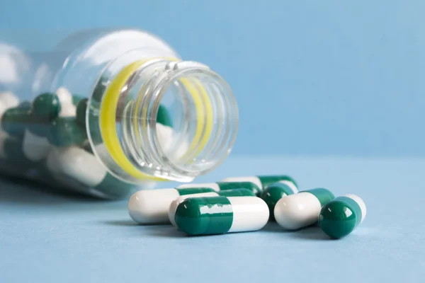 Green and white pills spill out of a plastic jar on blue backgro — Stock Photo, Image