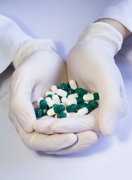 Hands in medical rubber gloves holding green and white capsules — Stock Photo, Image