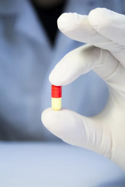 Close-up mão em luva de borracha médica segurando um vermelho e amarelo — Fotografia de Stock