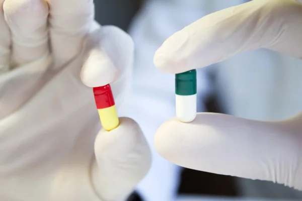 Hands in medical gloves holding different capsules — Stock Photo, Image