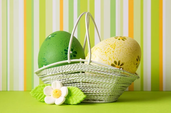 Green and yellow Easter eggs in a basket with white flower — Stock Photo, Image