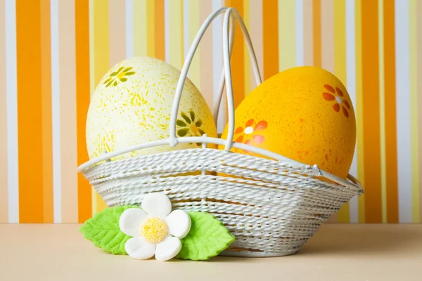 Uova di Pasqua gialle e arancioni in un cesto con fiore bianco — Foto Stock