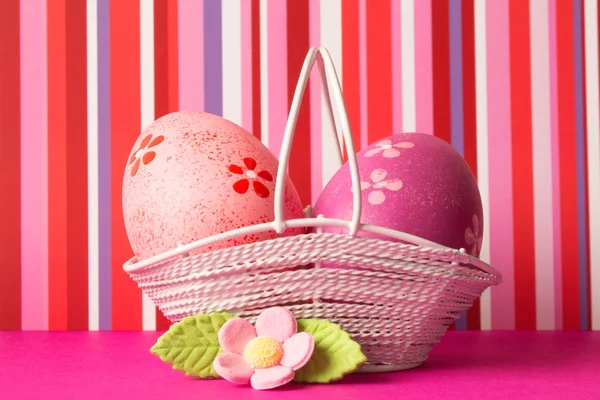 Huevos de Pascua rosados y carmesí en una canasta con flor rosa — Foto de Stock