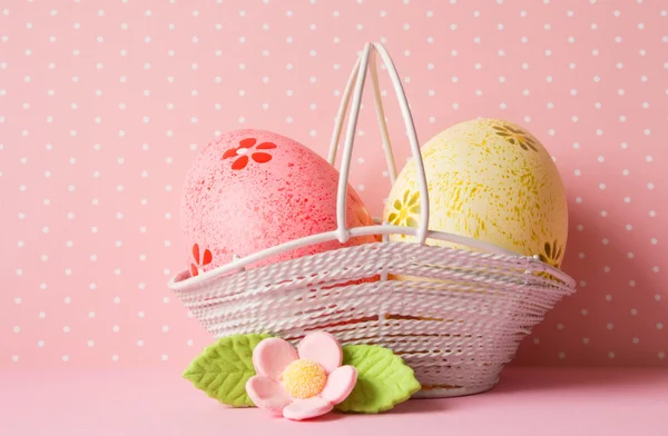 Huevos de Pascua rosados y amarillos en una cesta con flor rosa — Foto de Stock
