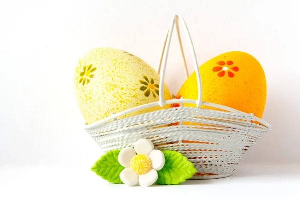 Orange and yellow Easter eggs in a basket with white flower — Stock Photo, Image