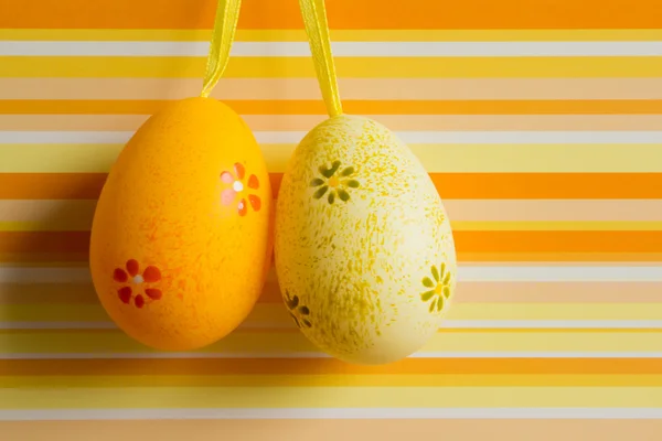 Orange und gelb aufgehängte Ostereier auf gestreiftem Hintergrund — Stockfoto