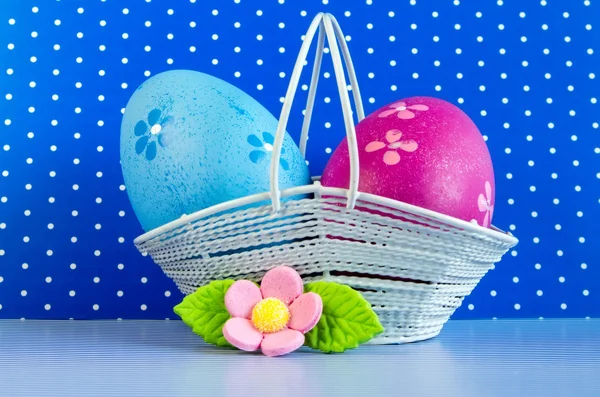 Uova di Pasqua blu e cremisi in un cesto con fiore rosa — Foto Stock