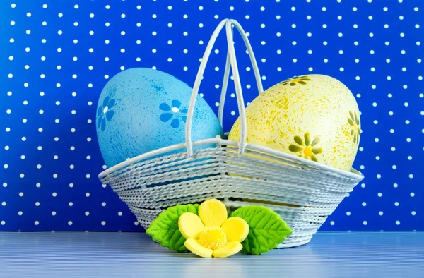 Uova di Pasqua blu e gialle in un cesto con fiore giallo — Foto Stock