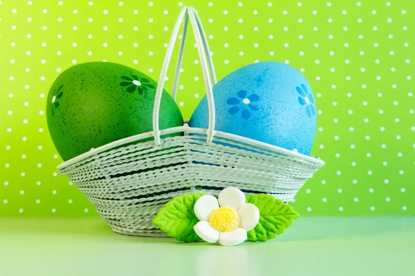Uova di Pasqua verdi e blu in un cesto con fiore bianco — Foto Stock