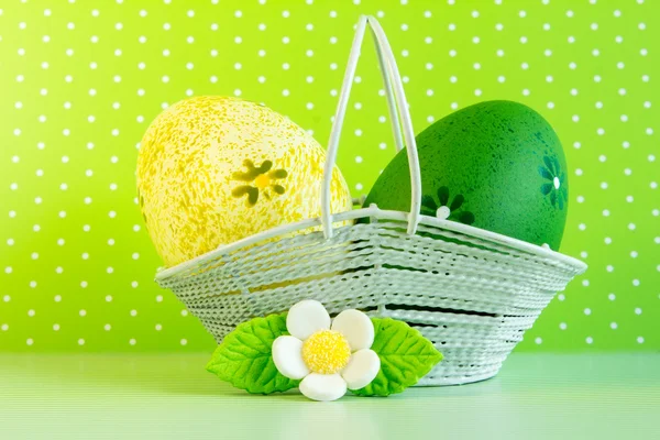 Uova di Pasqua gialle e verdi in un cesto con fiore bianco — Foto Stock