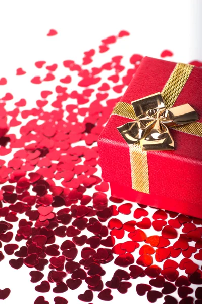 Красная подарочная коробка с золотым бантом и много красных сердечек на белом — стоковое фото