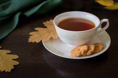 Koyu arka planda sarı meşe yapraklı kurabiyeli siyah çay. Yukarıdan bak. Fotoğraf seçici bir odak ile çekilir ve gürültü etkisi vardır..