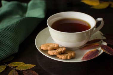 Koyu arka planda sarı meşe yapraklı kurabiyeli siyah çay. Yukarıdan bak. Fotoğraf seçici bir odak ile çekilir ve gürültü etkisi vardır..