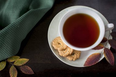 Koyu arka planda sarı meşe yapraklı kurabiyeli siyah çay. Yukarıdan bak. Fotoğraf seçici bir odak ile çekilir ve gürültü etkisi vardır..