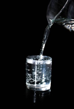 Siyah arka planda bir bardak dolusu su. Bir sürahide su akıyor. Fotoğraf seçici odak ve gürültü efektiyle çekildi