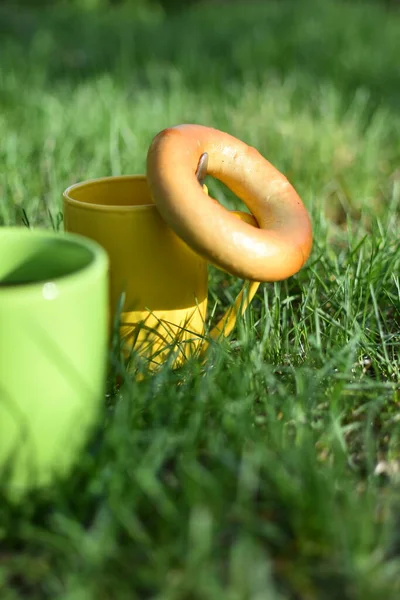 绿色的草地上站着黄色和绿色的杯子 附近是一个百吉饼 有选择地拍照 — 图库照片