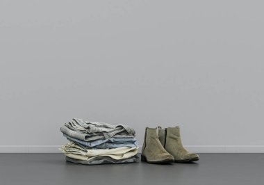 Süet erkek ayakkabıları ve yerde katlanmış çamaşırları. Gri bir iç odada, içinde fotokopi alanı olan kumaş ve aksesuarlar.