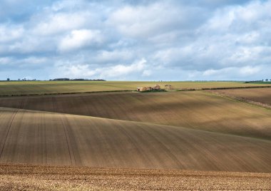 Güneşli bir günde bulutlu bir havada, tarlalı tarlaların üzerinde deralict bir çiftlik manzarası.