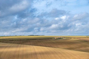Güneşli bir günde bulutlu bir havada, tarlalı tarlaların üzerinde deralict bir çiftlik manzarası.