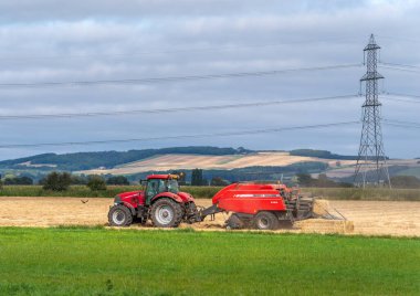 İngiltere, Yorkshire, Beilby, 20 / 09 / 2020 - Kırmızı Vaka Traktör güç hatlarının yanındaki tarlada bir Massey Ferguson balyası ile saman balyalama