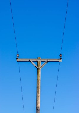 Mavi arka planlı, ahşap bir telgraf direğindeki yalıtıcılarda iki elektrik hattı.