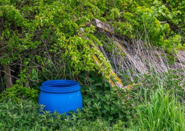 Mavi plastik fıçı bir tarlanın kenarındaki çitin içine yerleştirilmiş..
