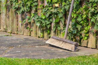 Arkasında sarmaşık olan bir bahçe ortamında tahta bir süpürge başı ve sapı..