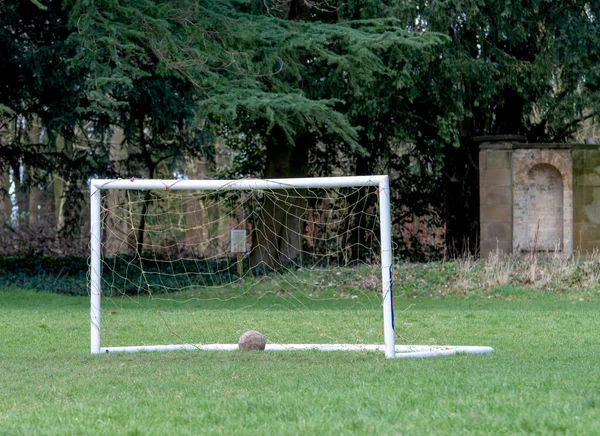 Small 5 a side goal posts with a ball on the ground with trees in the background.