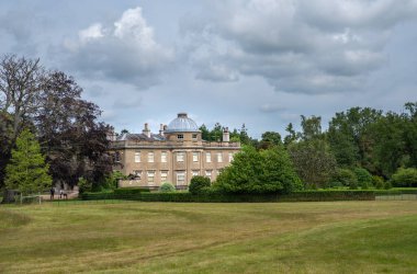 Scampston, Malton, North Yorkshire, UK, 07 July 2021 - Looking over grass lawn to Scampston Hall with trees and cloudy sky