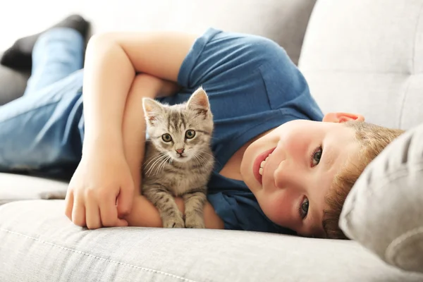 Kind mit Kätzchen auf grauem Sofa — Stockfoto