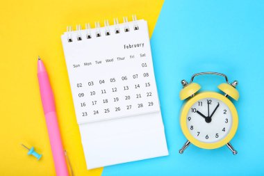 Renkli kağıt zemin üzerinde alarm saati ve kalemle takvim sayfası