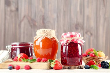 Cam kavanozlarda reçel ve ahşap arka planda taze böğürtlen.