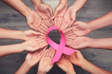 Göğüs kanseri konsepti. Bir grup insan ellerinde kahverengi ahşap arka planda pembe bir kurdele tutuyor.