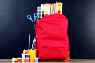 Siyah arka planda okul malzemeleriyle dolu sırt çantası.
