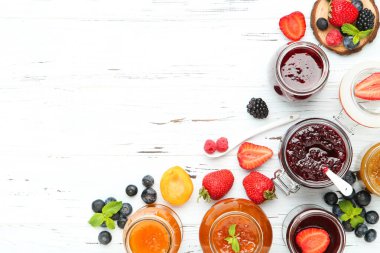 Cam kavanozlarda tatlı reçel, olgun böğürtlenler beyaz ahşap masada.