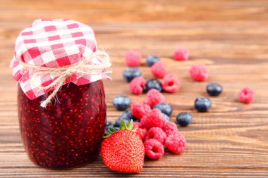 Cam kavanozda tatlı reçel, kahverengi ahşap arka planda olgun böğürtlen.