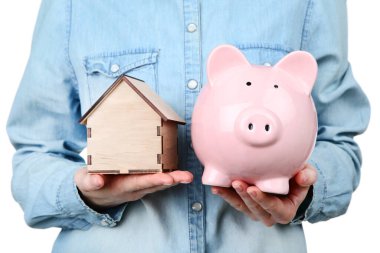 Ahşap ev modeli ve pembe kumbara taşıyan bir kadın.