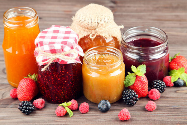 Sweet jam in glass jars with berries on wooden table
