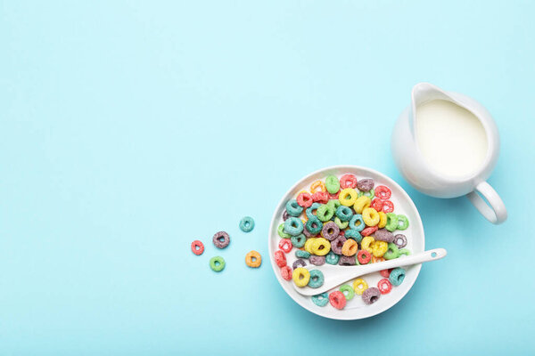 Colorful corn rings in bowl with milk and spoon on blue background